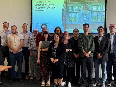 A group of men and women stand in front of a screen smiling at the camera in a university teaching room